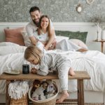 A family enjoying a relaxed morning in a cozy bedroom with a toddler playing.