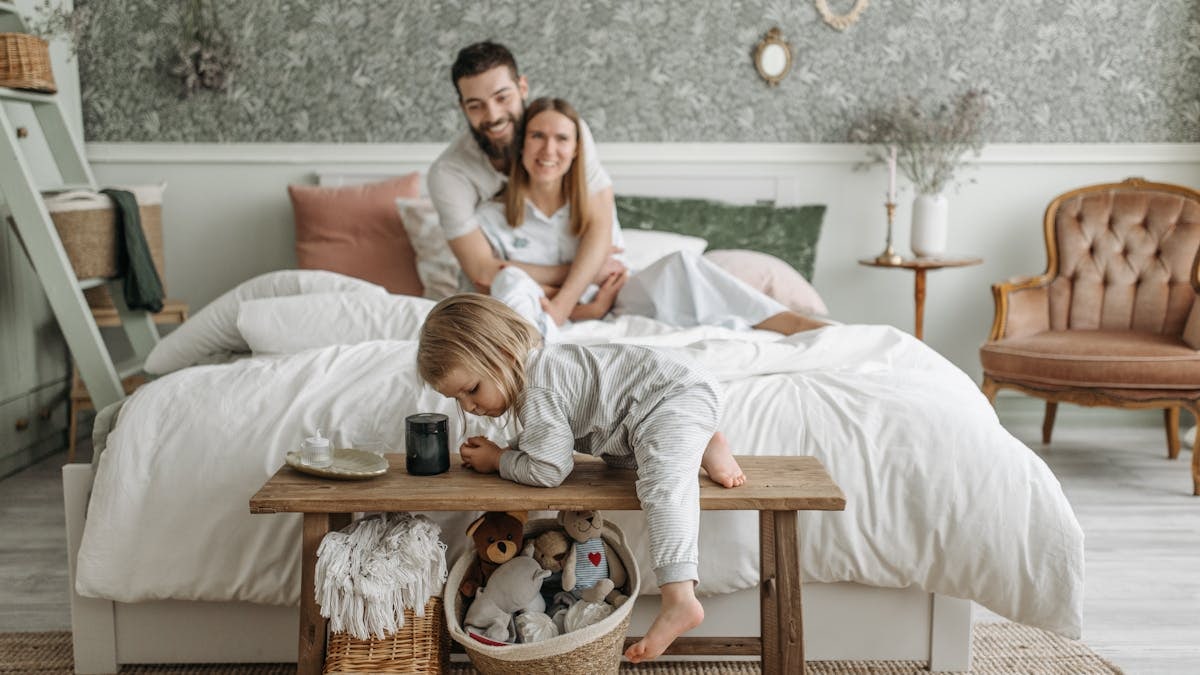 A family enjoying a relaxed morning in a cozy bedroom with a toddler playing.